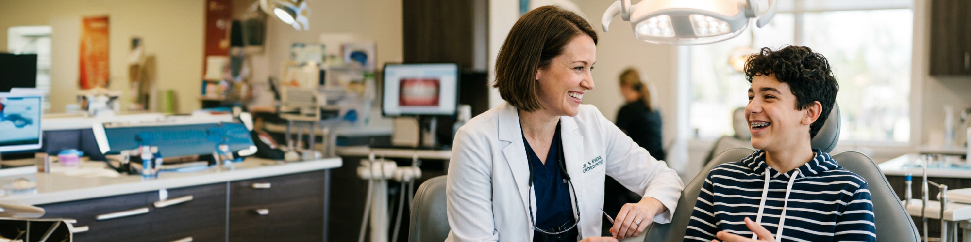 Female dentist conversing with young male patient in dental office.